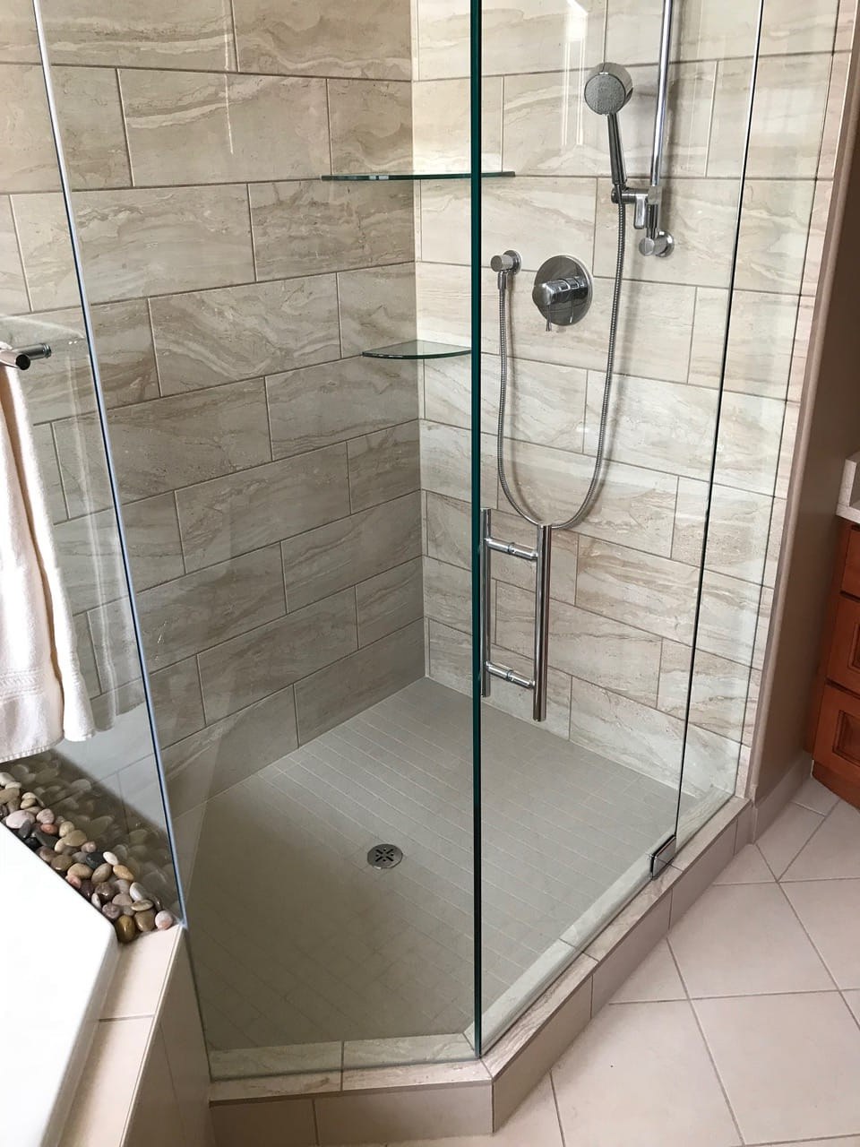 Frameless neo-angle glass shower with travertine-look tile and handheld sprayer